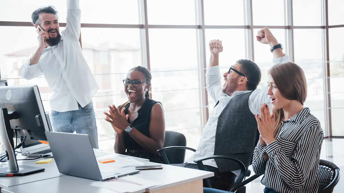 Employees in office setting celebrating at computer desk